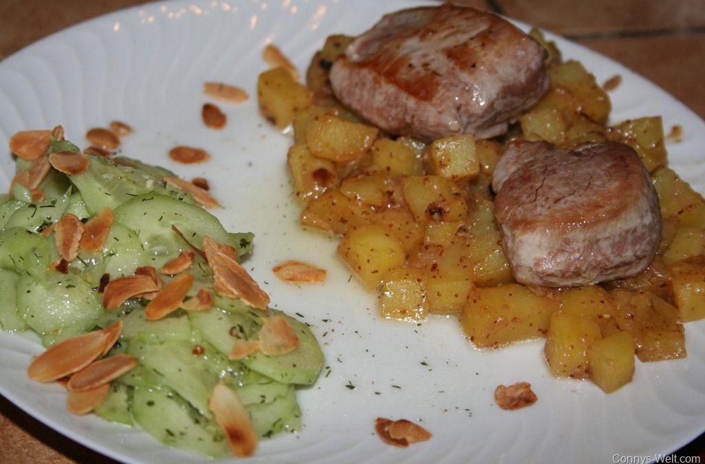 Zarte Schweinemedaillons auf Kartoffeln in süßer Senf-Soße und feinem Mandel-Gurken-Salat